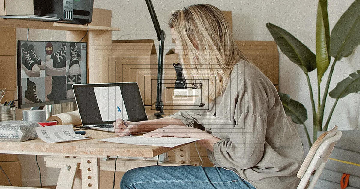A woman using her phone at a desk, surrounded by art supplies and a laptop, in a creative workspace. — Foto: Andrea Piacquadio / Pexels